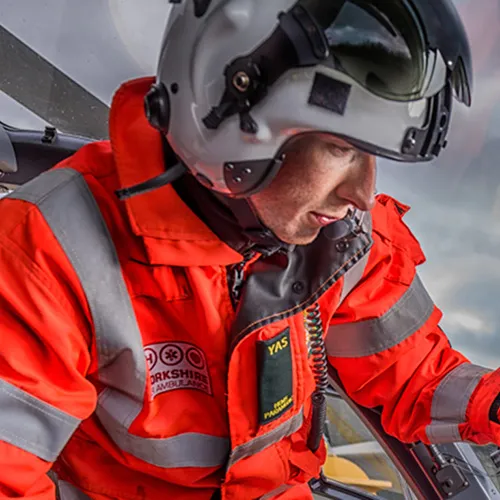 A person in a reflective orange suit and helmet is inside what appears to be a helicopter cockpit, focused on something.